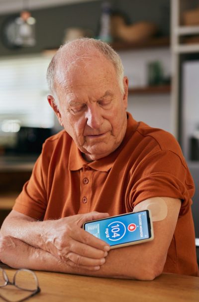 Elderly man using digital sensor to measure blood sugar levels at home. Senior monitoring glucose levels with a digital medical sensor device. Old man with diabetes using smart remote sensor and smartphone for controlling and monitoring blood sugar level at home.