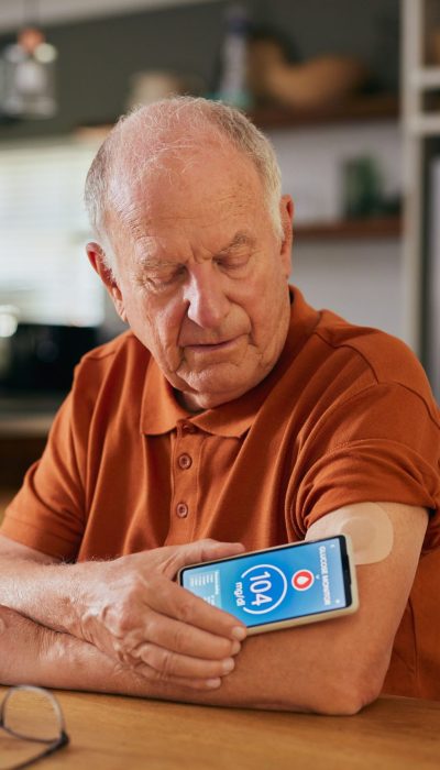 Elderly man using digital sensor to measure blood sugar levels at home. Senior monitoring glucose levels with a digital medical sensor device. Old man with diabetes using smart remote sensor and smartphone for controlling and monitoring blood sugar level at home.
